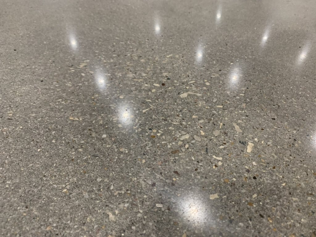 Polished concrete with salt-and-pepper aggregate exposure and high-gloss reflections