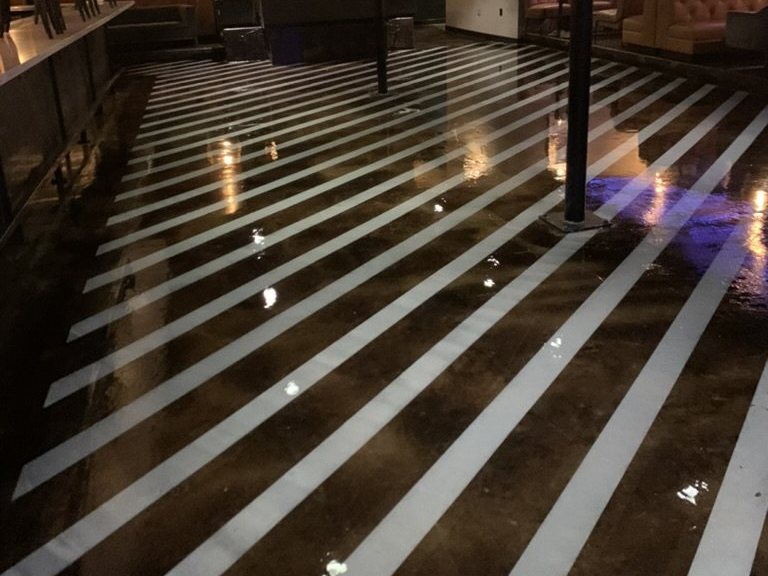 Stained and sealed concrete floor with custom white stripes in a bar and lounge